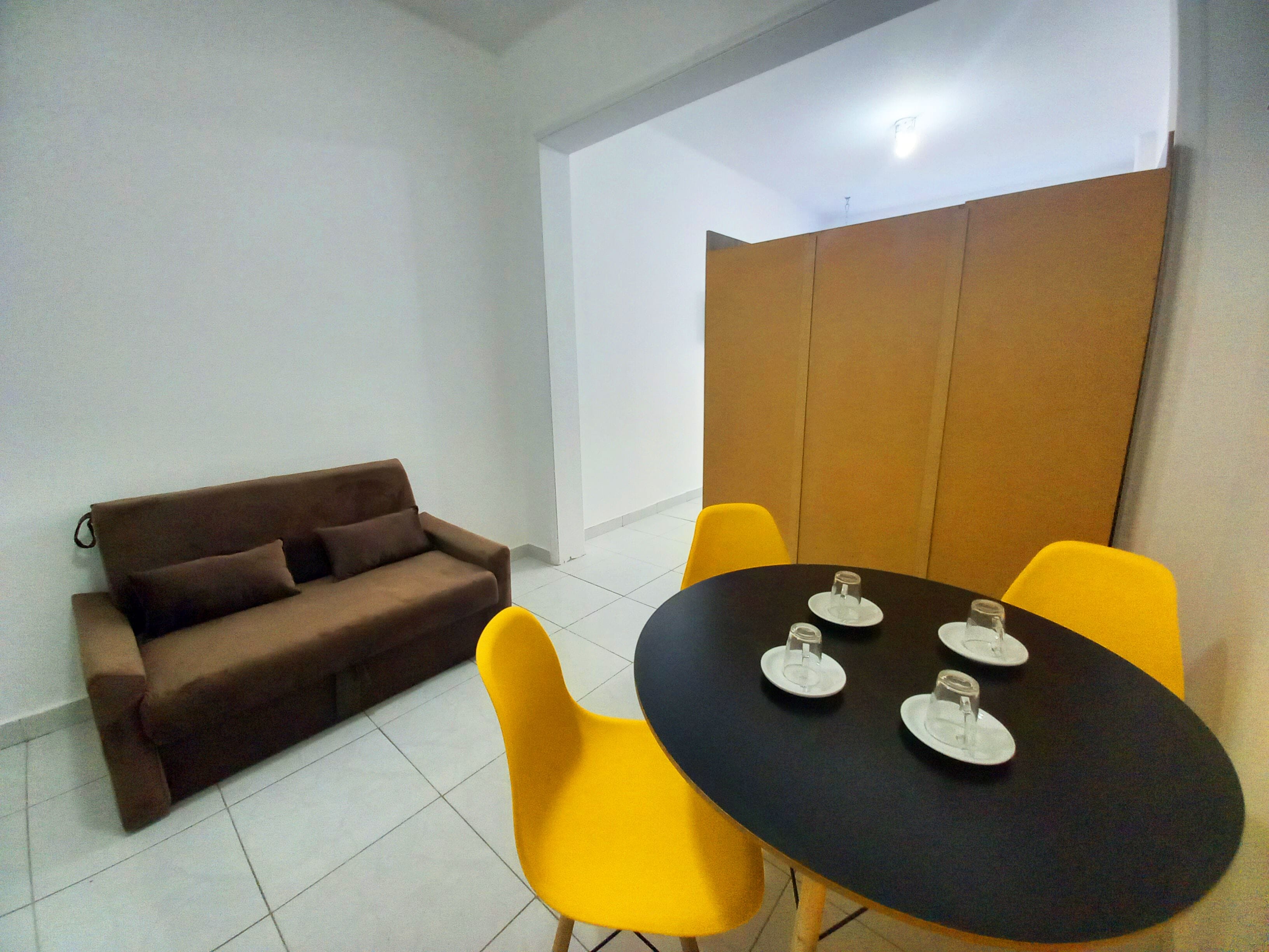 A small, modern room with a brown sofa, a black table with four chairs, and a white partition.