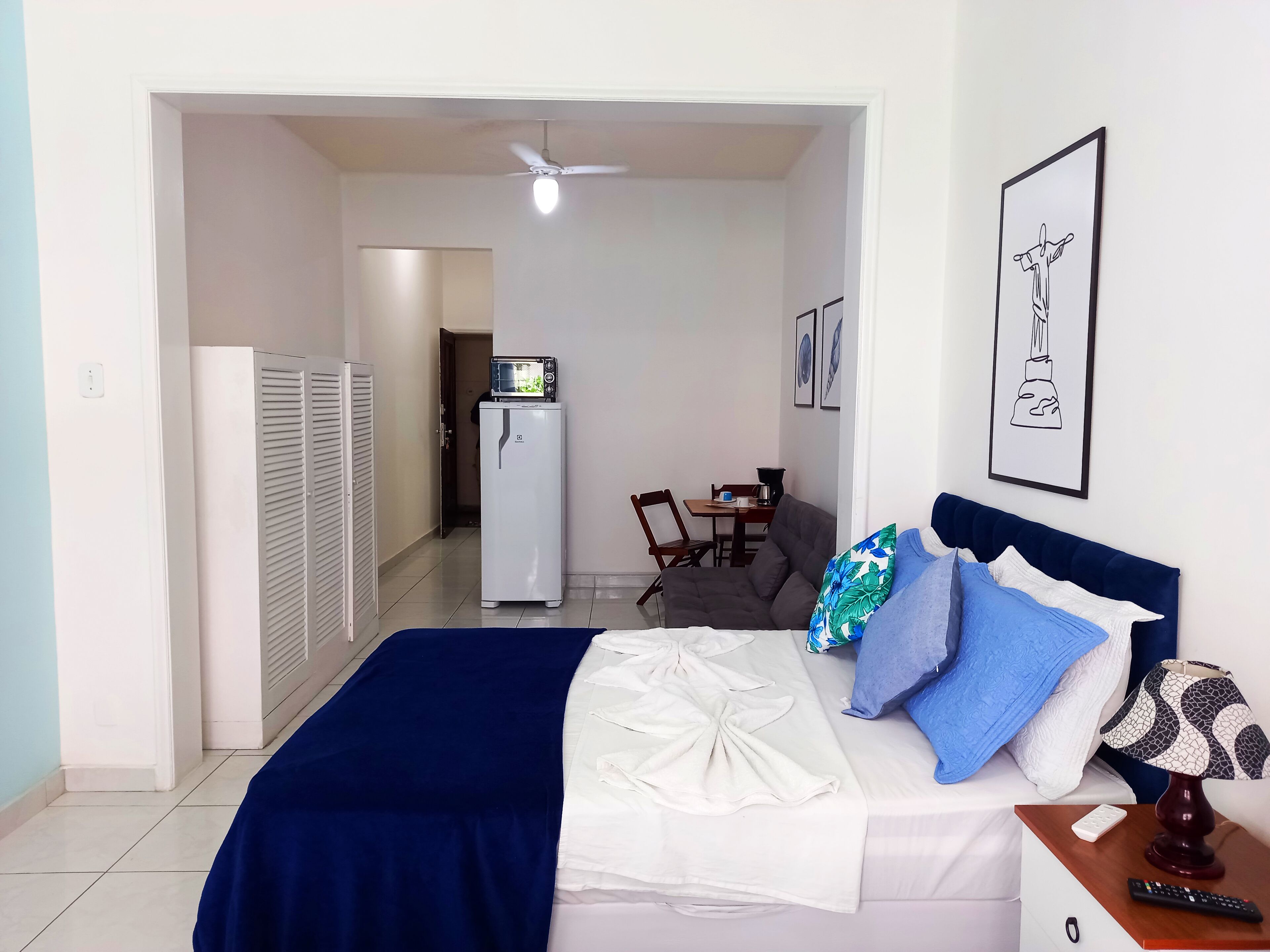 Ein Schlafzimmer mit Bett, Schreibtisch, Stuhl, Kühlschrank und Deckenventilator.
