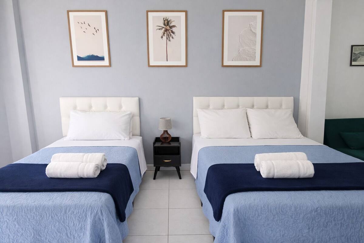 Una habitación de hotel con dos camas, una mesita de noche y tres cuadros en la pared.