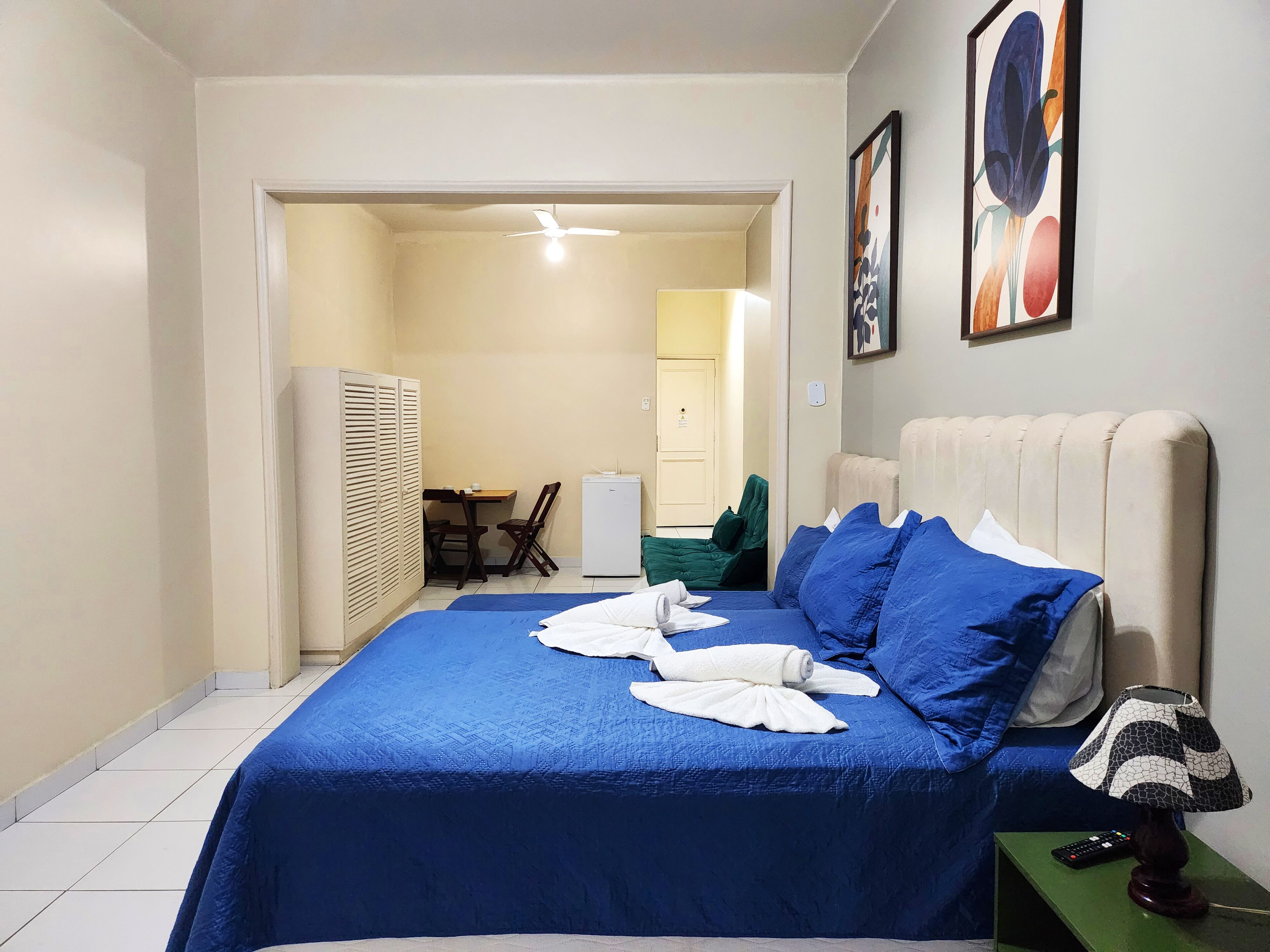 A hotel room with a bed, a desk, a chair, a wardrobe, and a door leading to another room.