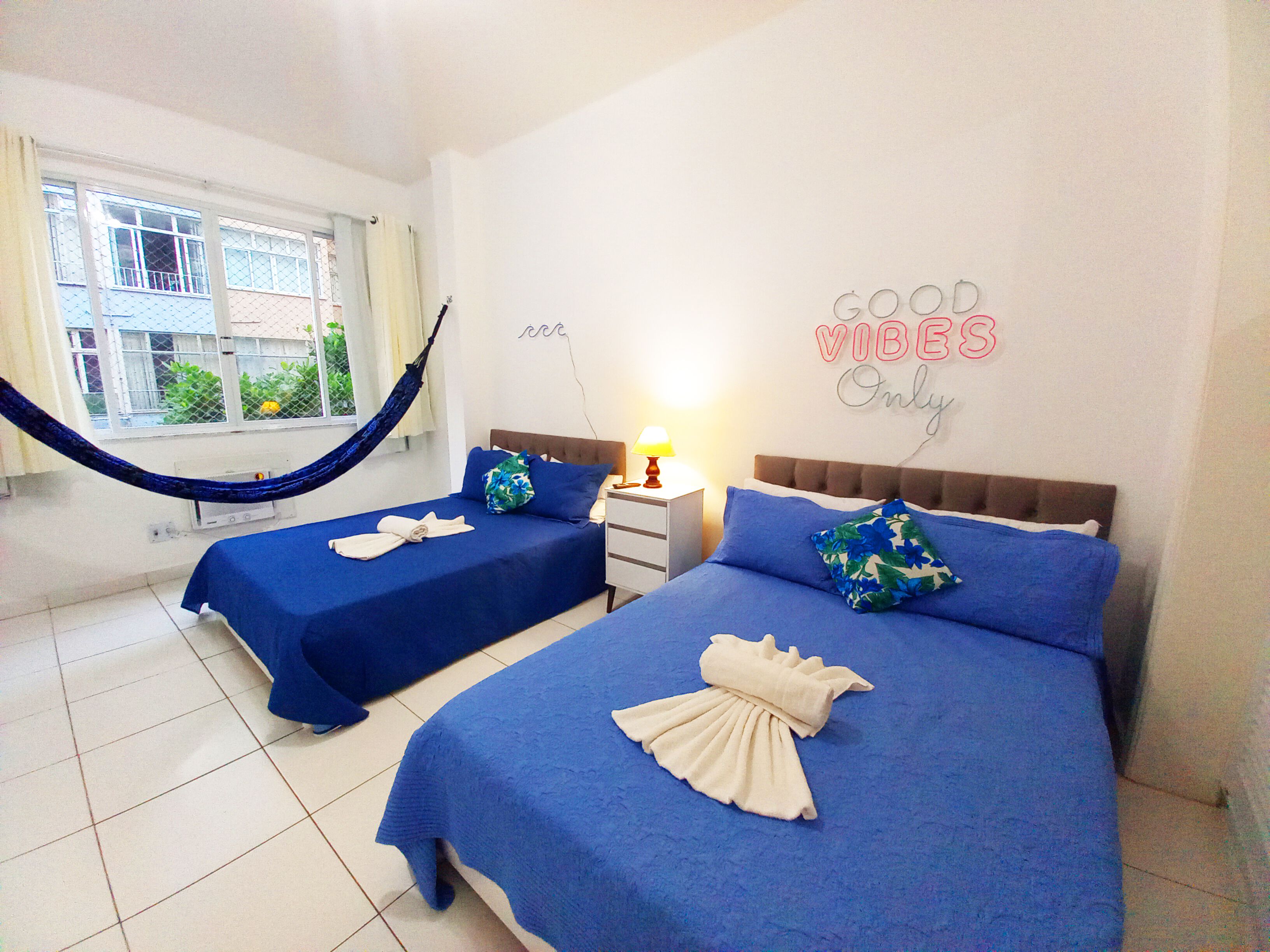 Een hotelkamer met twee bedden, een hangmat en een bordje met de tekst 'GOOD VIBES Only'.