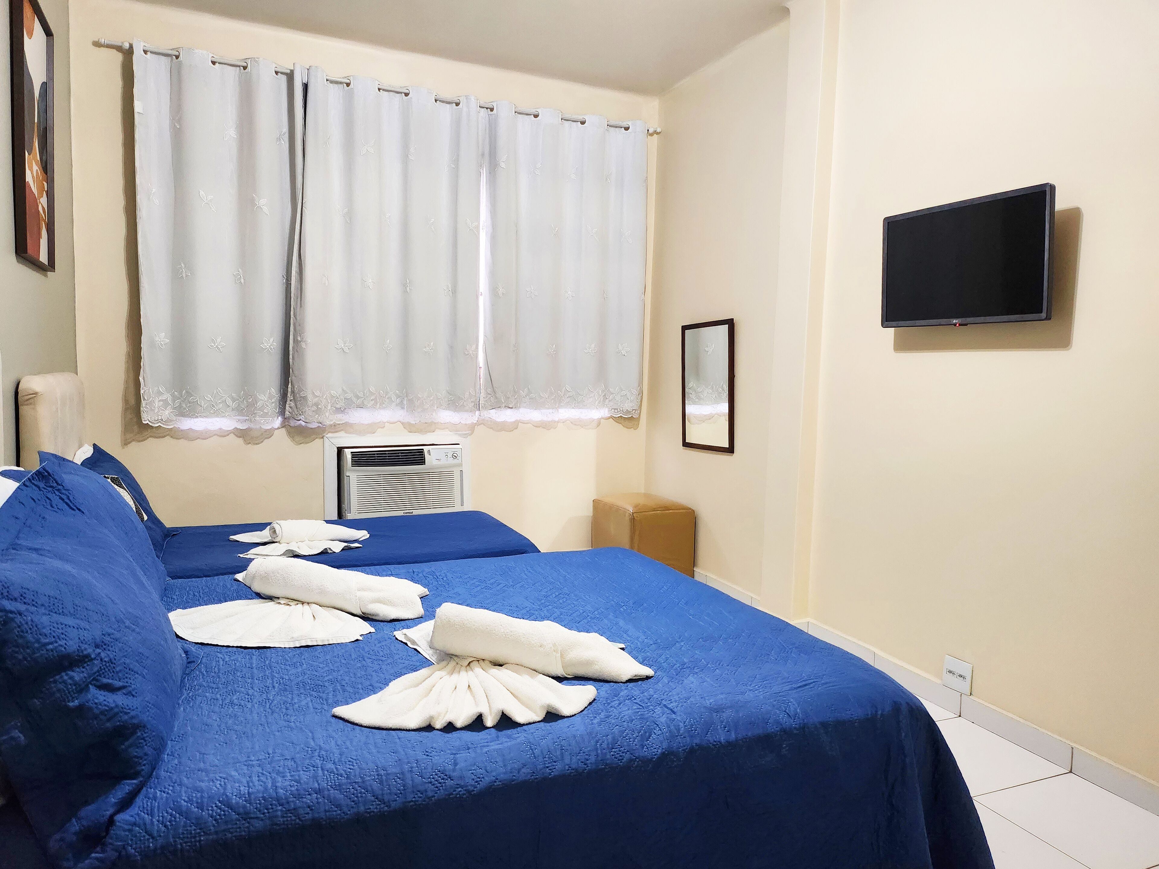 A hotel room with two beds, a TV, a mirror, and an air conditioning unit.