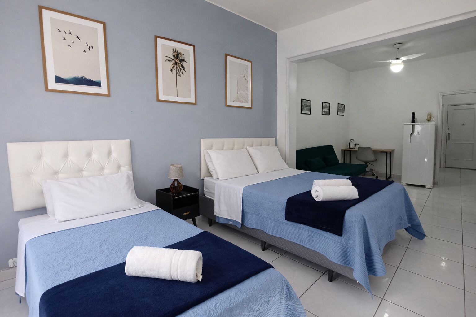 A hotel room with two beds, a desk, a chair, and a refrigerator.
