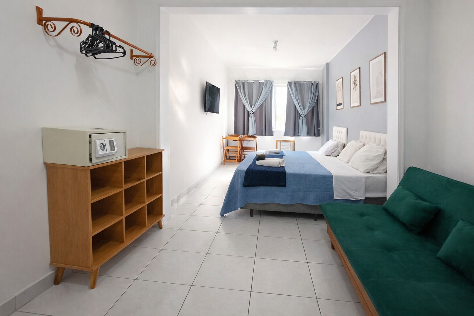 Ein Zimmer mit einem Bett, einem grünen Sofa, einem Holzbodenregal mit einem gerahmten Bild und einem Fernseher an der Wand.