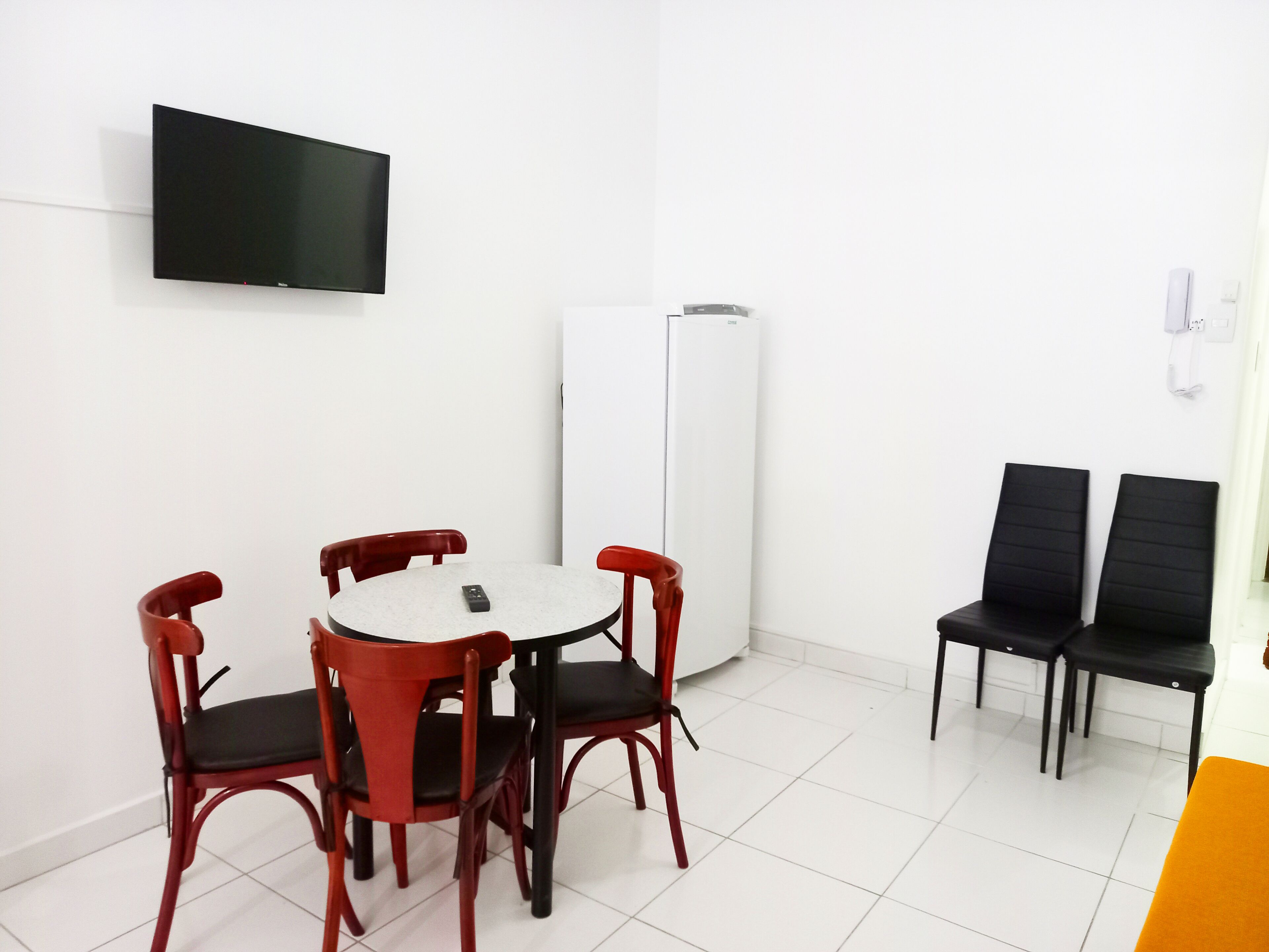 A small, modern room with a round table and four chairs, a flat-screen TV mounted on the wall, and a white air conditioning unit.