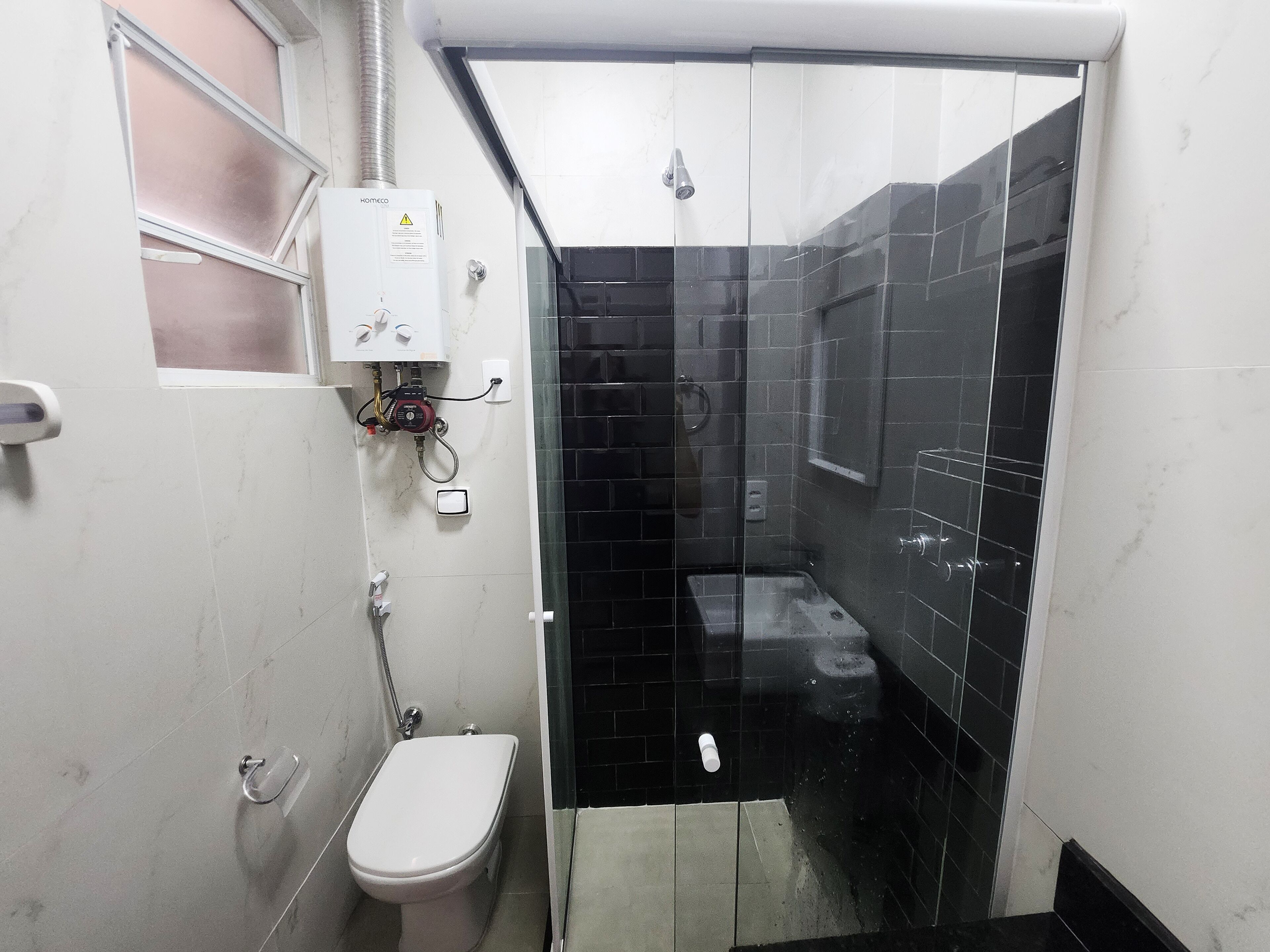 A compact bathroom with a toilet, a shower enclosure, and a built-in sink.