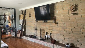 Un saló amb una llar de pedra, un televisor de pantalla plana muntat a la part superior i un sòl de fusta.