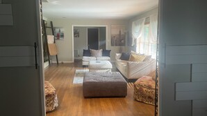 Un saló amb un sofà, un pouf i una taula de centre. Hi ha una porta que dona a una altra habitació.