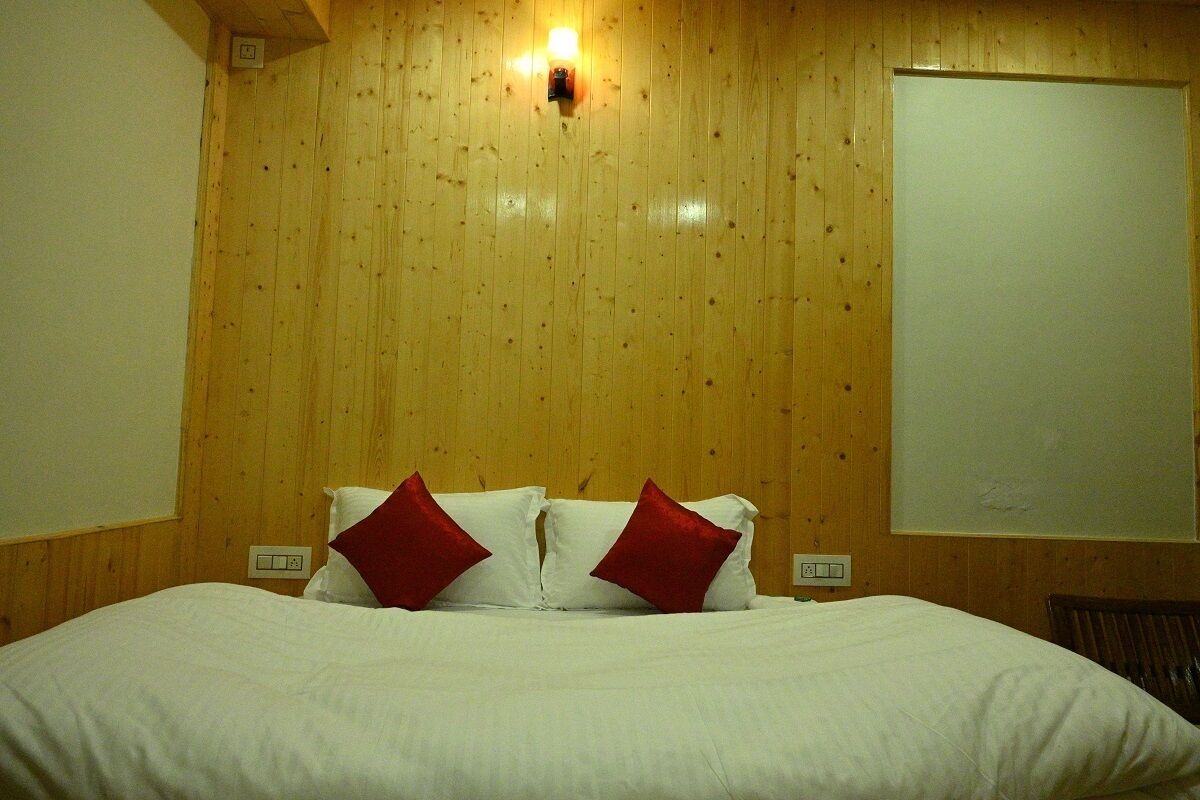 A hotel room with a wooden paneled wall, a bed with white bedding and red pillows, and a whiteboard on the wall.