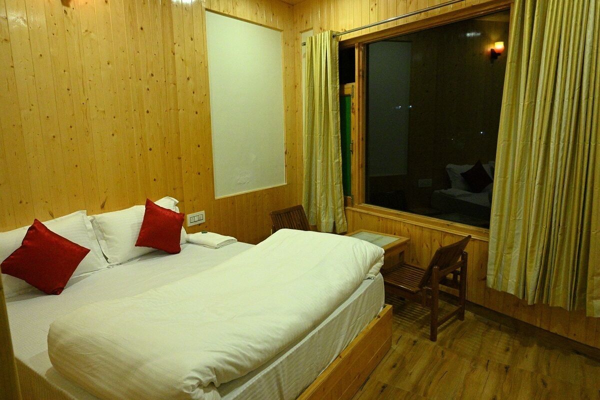 A wooden-paneled room with a bed, a chair, a window, and a curtain.