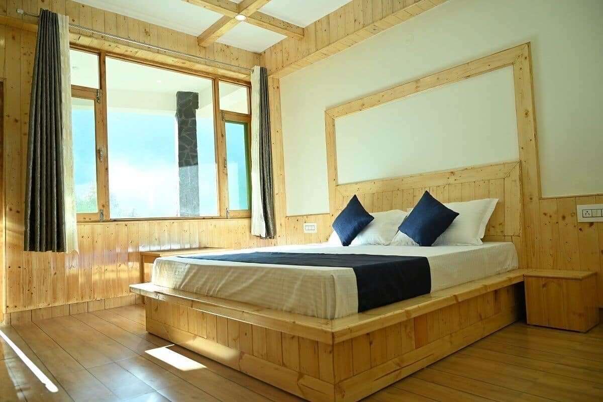 A wooden-paneled bedroom with a large bed, a stone fireplace, and a view through the window.