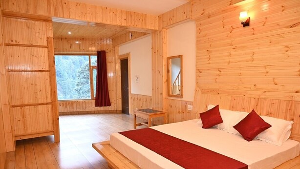 Ein Schlafzimmer mit Holzwänden, einem großen Bett, einem kleinen Tisch und einem Fenster mit Blick auf Bäume.