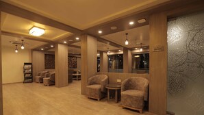 Un'ampia hall con pavimento in legno, diverse zone relax e un'area riservata segnalata da un cartello.