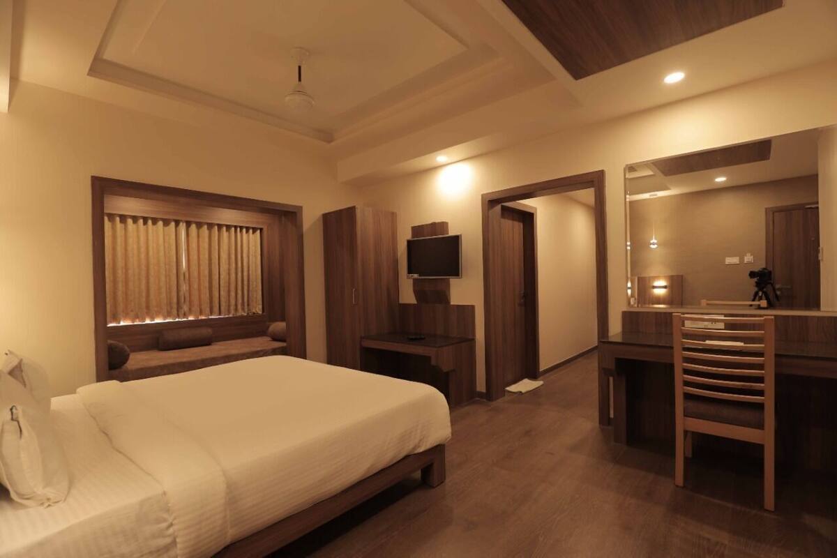 A hotel room with a bed, a desk, a chair, a TV, and a mirror.