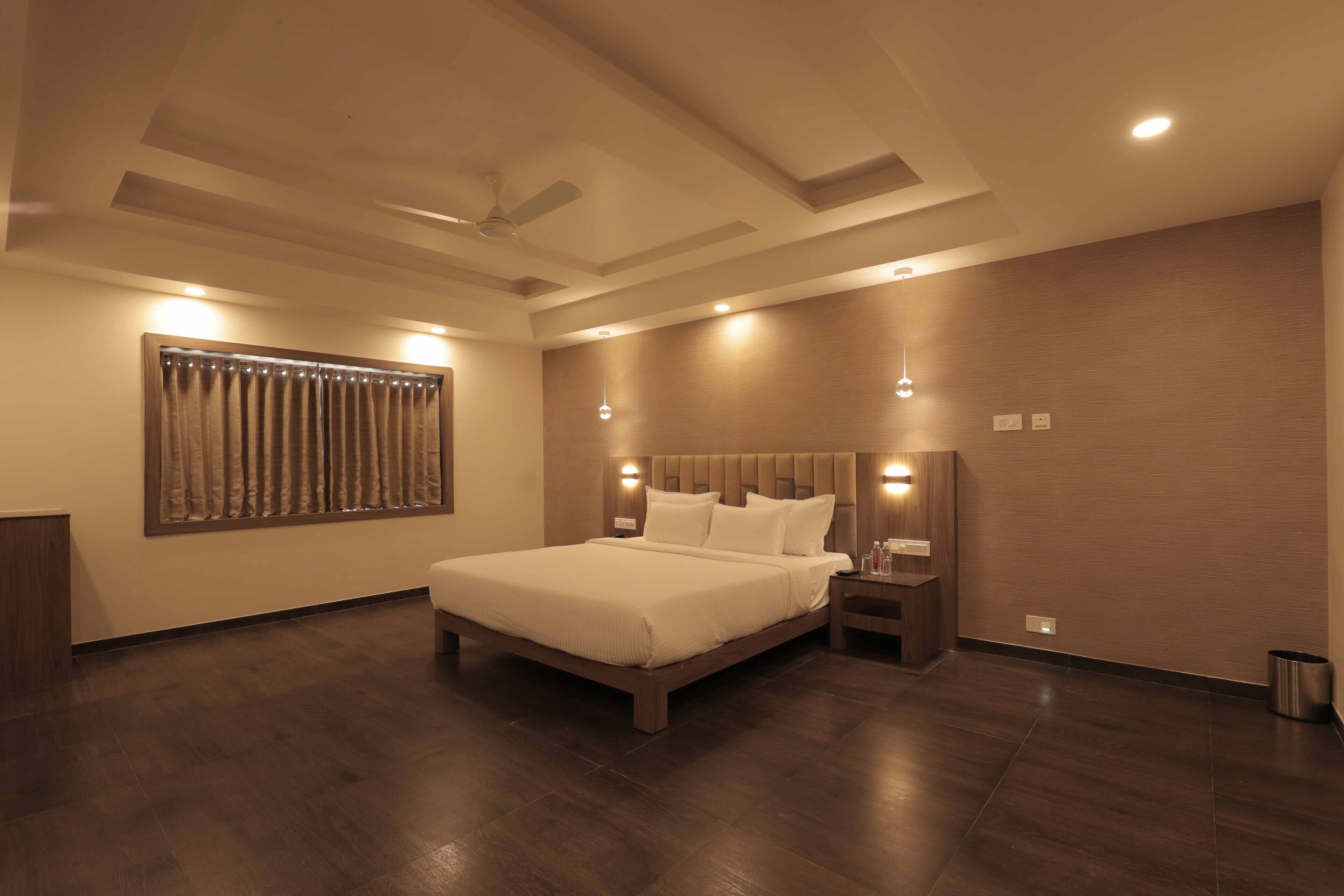 A modern bedroom with a large bed, wooden flooring, a ceiling fan, and recessed lighting.