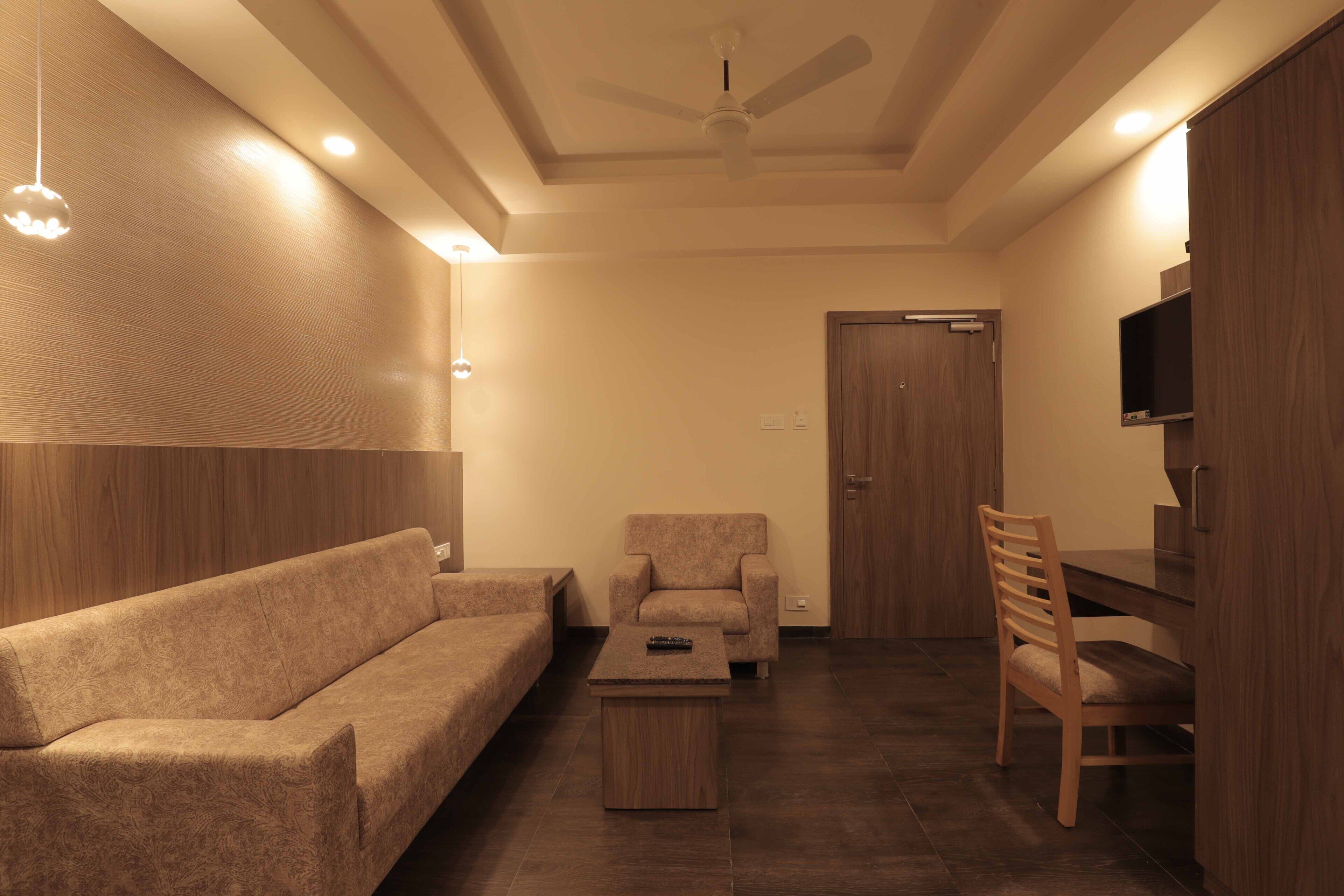 Una sala de estar con sofá, sillón, mesa de centro y televisor montado en la pared.