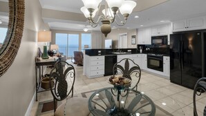 A modern kitchen with a central island, black appliances, and a dining area with a glass table. - 2311-23rd Flr-Outdoor Pool-Poolside Cafe-Hot Tub-Grills-AMAZING Birds Eye VIEW! (Panama City Beach)