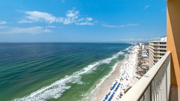 A beach with a row of blue umbrellas and a building with balconies overlooking the ocean. - 2311-23rd Flr-Outdoor Pool-Poolside Cafe-Hot Tub-Grills-AMAZING Birds Eye VIEW! (Panama City Beach)