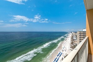 A beach with a row of blue umbrellas and a building with balconies overlooking the ocean.