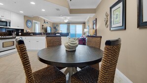 A modern kitchen with white cabinets, a round dining table with woven chairs, and a chandelier. - 1806-18th Floor-2 Bedroom-Heated Pool-HOT TUB-GRILLS-AMAZING BEACH FRONT VIEWS (Panama City Beach)