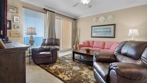 A living room with a brown leather sofa, a pink sofa, a wooden coffee table, and a ceiling fan. - 1806-18th Floor-2 Bedroom-Heated Pool-HOT TUB-GRILLS-AMAZING BEACH FRONT VIEWS (Panama City Beach)