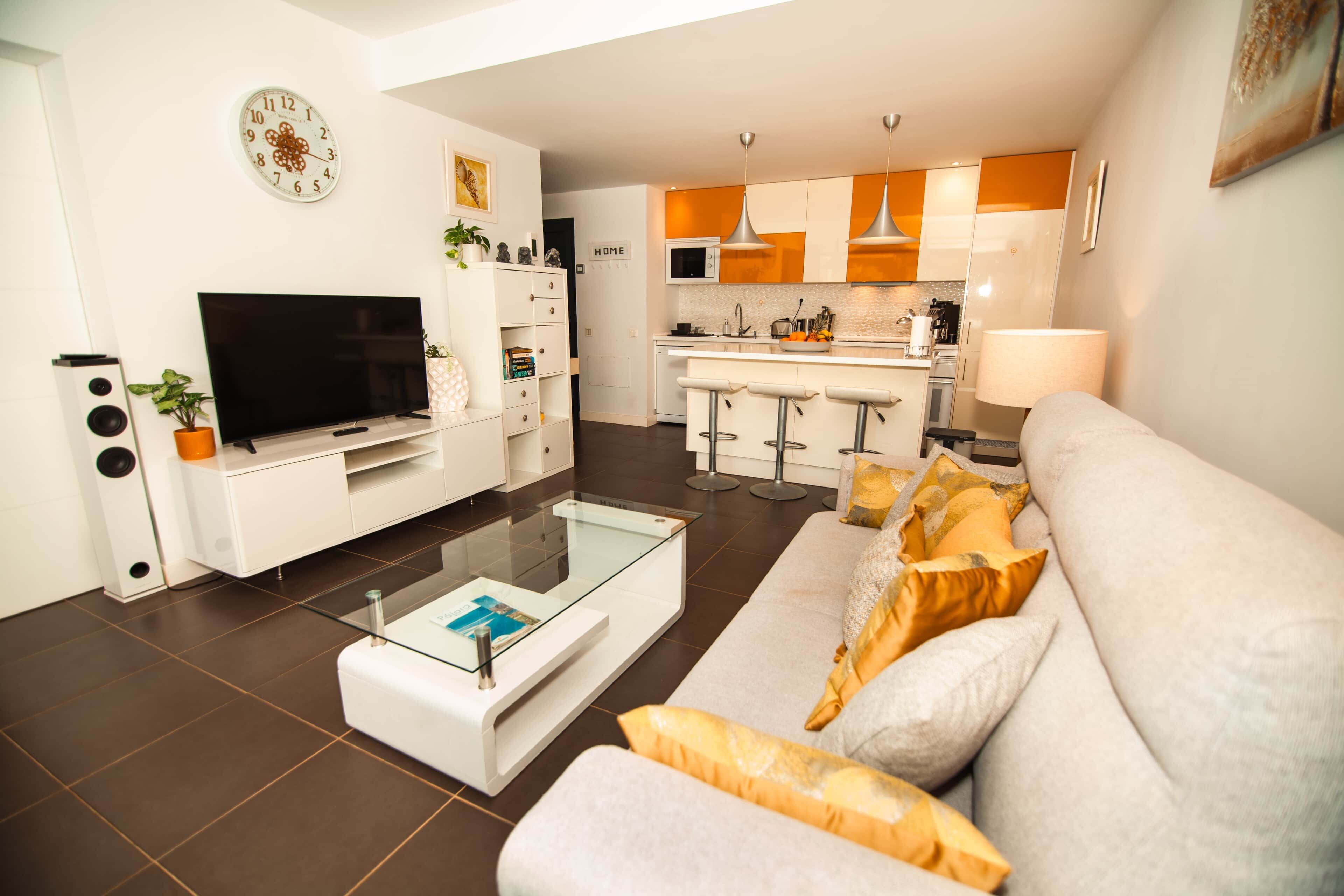 A modern living room with a flat-screen TV, a glass coffee table, and a sofa with cushions.