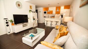 A modern living room with a flat-screen TV, a glass coffee table, and a sofa with cushions.