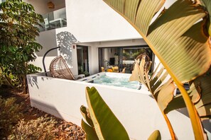 A modern outdoor hot tub area with a glass-enclosed dining space and a large plant in the foreground. - Luxury Ground Floor: Terrace, Hot Tub and Sauna (La Oliva)
