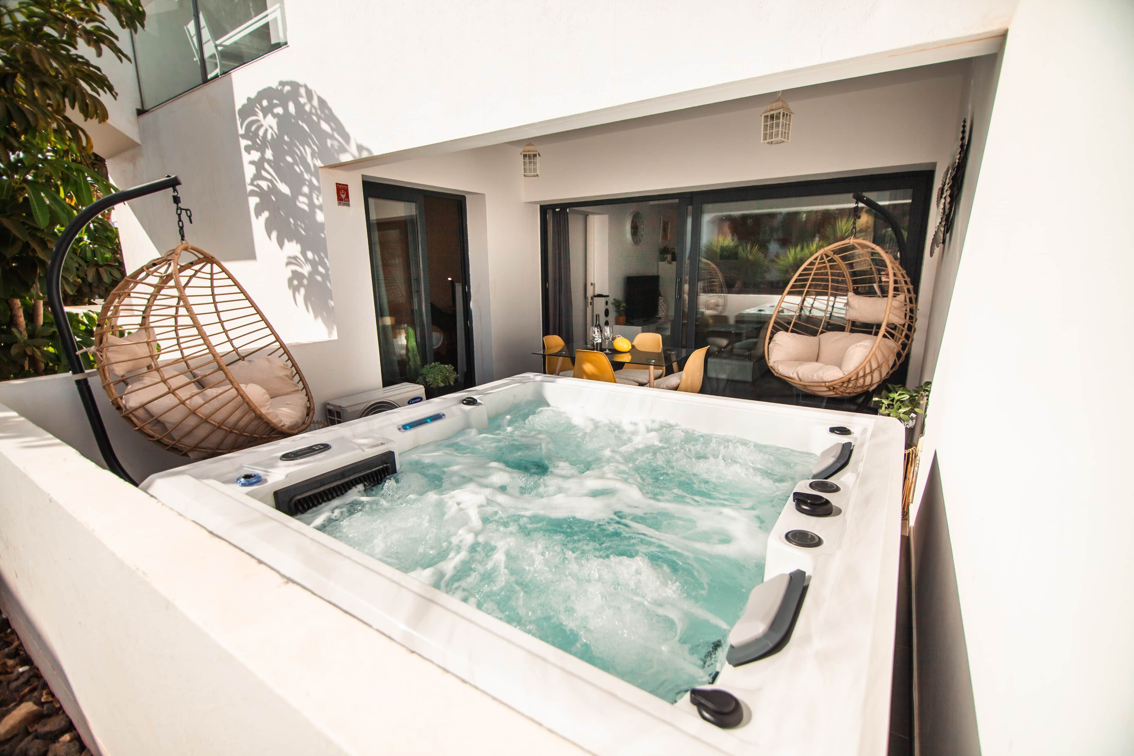 Ein Whirlpool mit zwei Korbstühlen, einer Glastür und einem kleinen Tisch mit Flaschen und Gläsern.