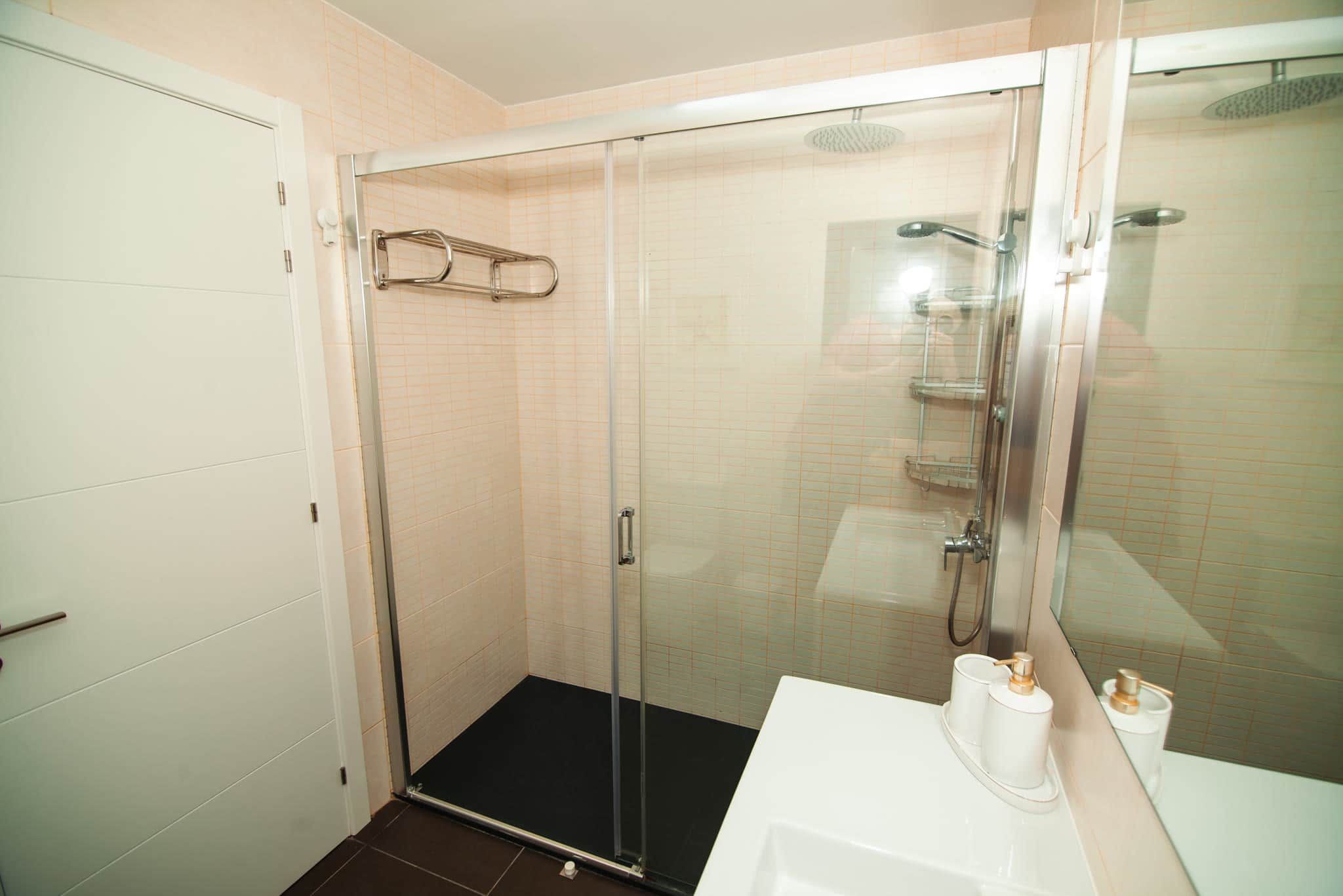 Una doccia con pareti in vetro, un lavandino bianco e articoli da toilette.