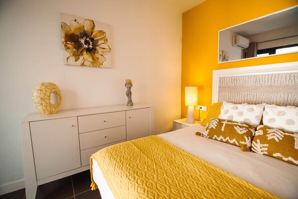 A bedroom with a bed, bedside table, lamp, and a wall-mounted mirror.