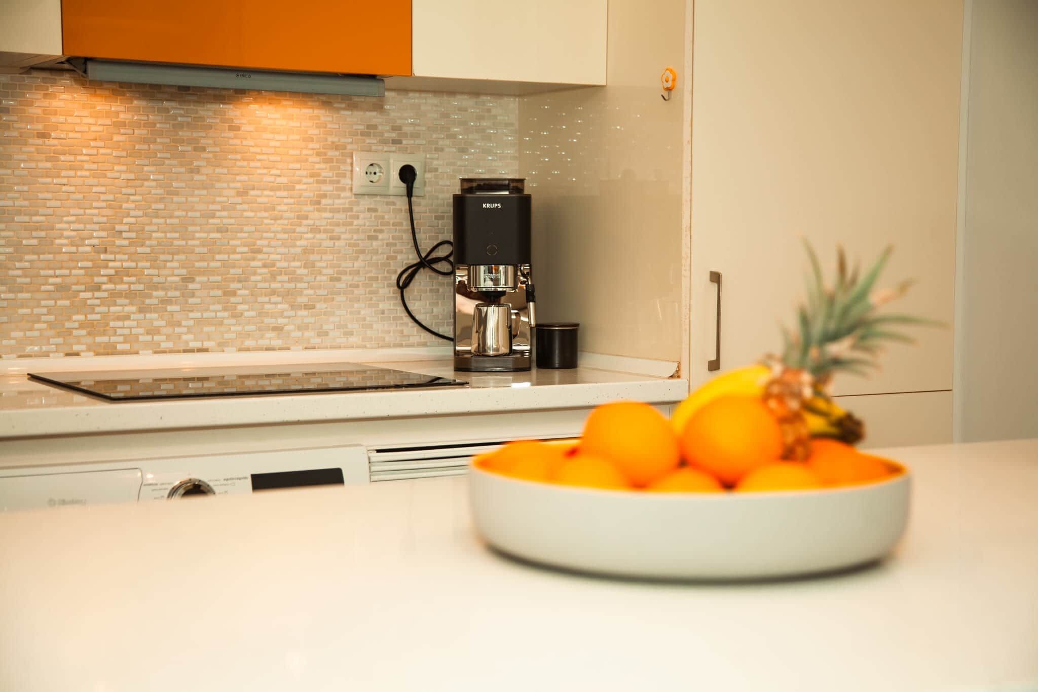 Une cuisine avec une machine à café, un saladier rempli d’oranges et une plante en pot.