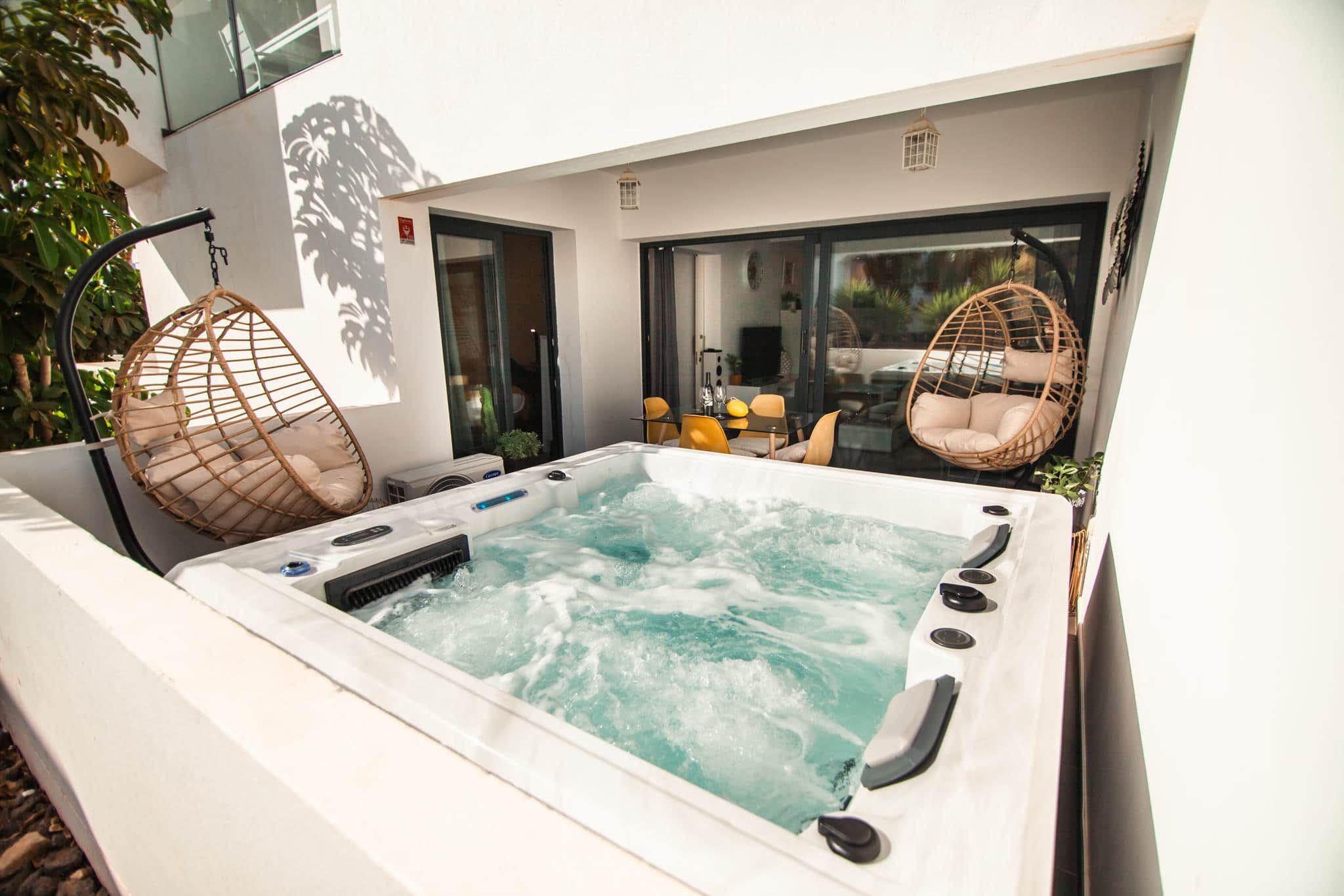 Een jacuzzi met glazen omheining, omgeven door zitplaatsen buiten en een modern gevelontwerp.