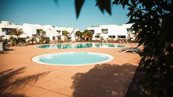 Una piscina con sillas de descanso y palmeras, rodeada de edificios blancos modernos.