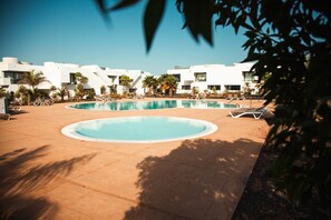 Ein Swimmingpool mit Liegestühlen und Palmen, umgeben von modernen, weißen Gebäuden.