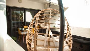 A wicker hanging chair with cushions, a glass table, and chairs in a modern outdoor setting.