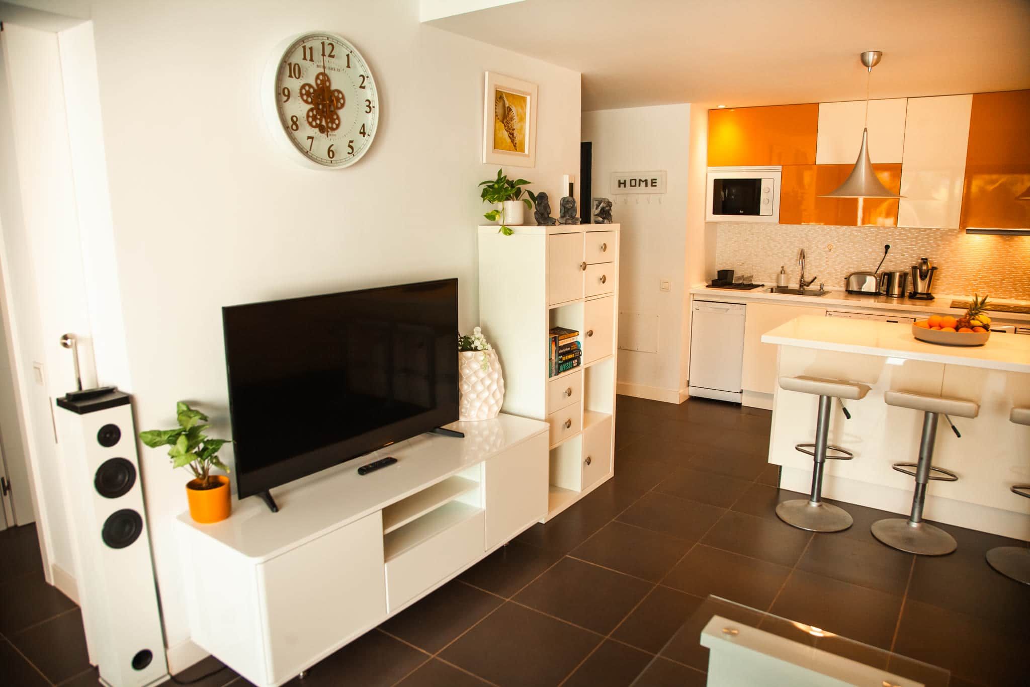 A modern kitchen with white cabinets, a built-in oven, and a bar area with stools.