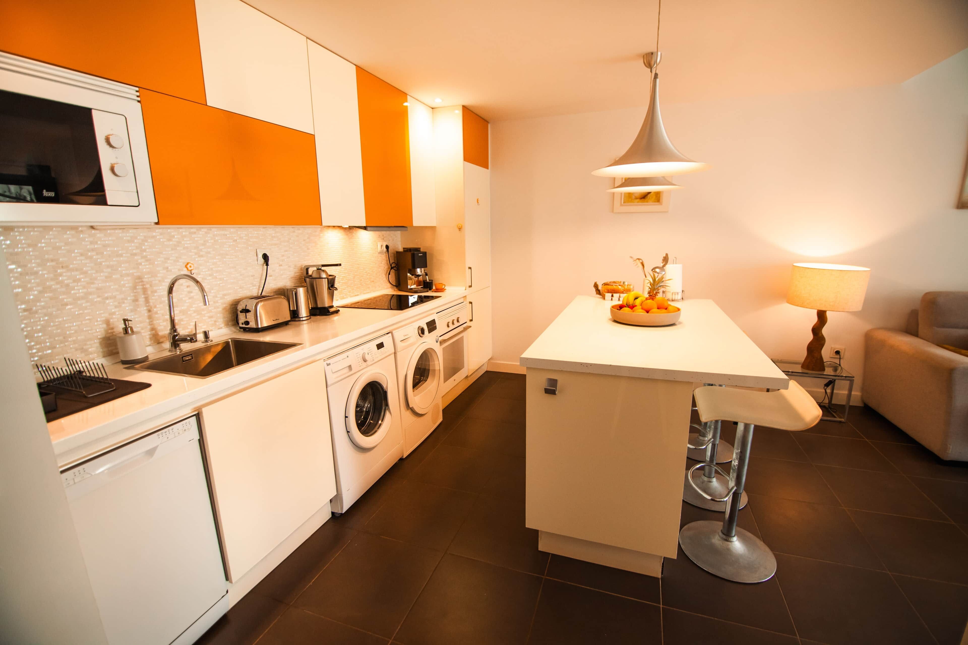 Una cocina moderna con lavadora integrada, cafetera y comedor con mesa y sillas.