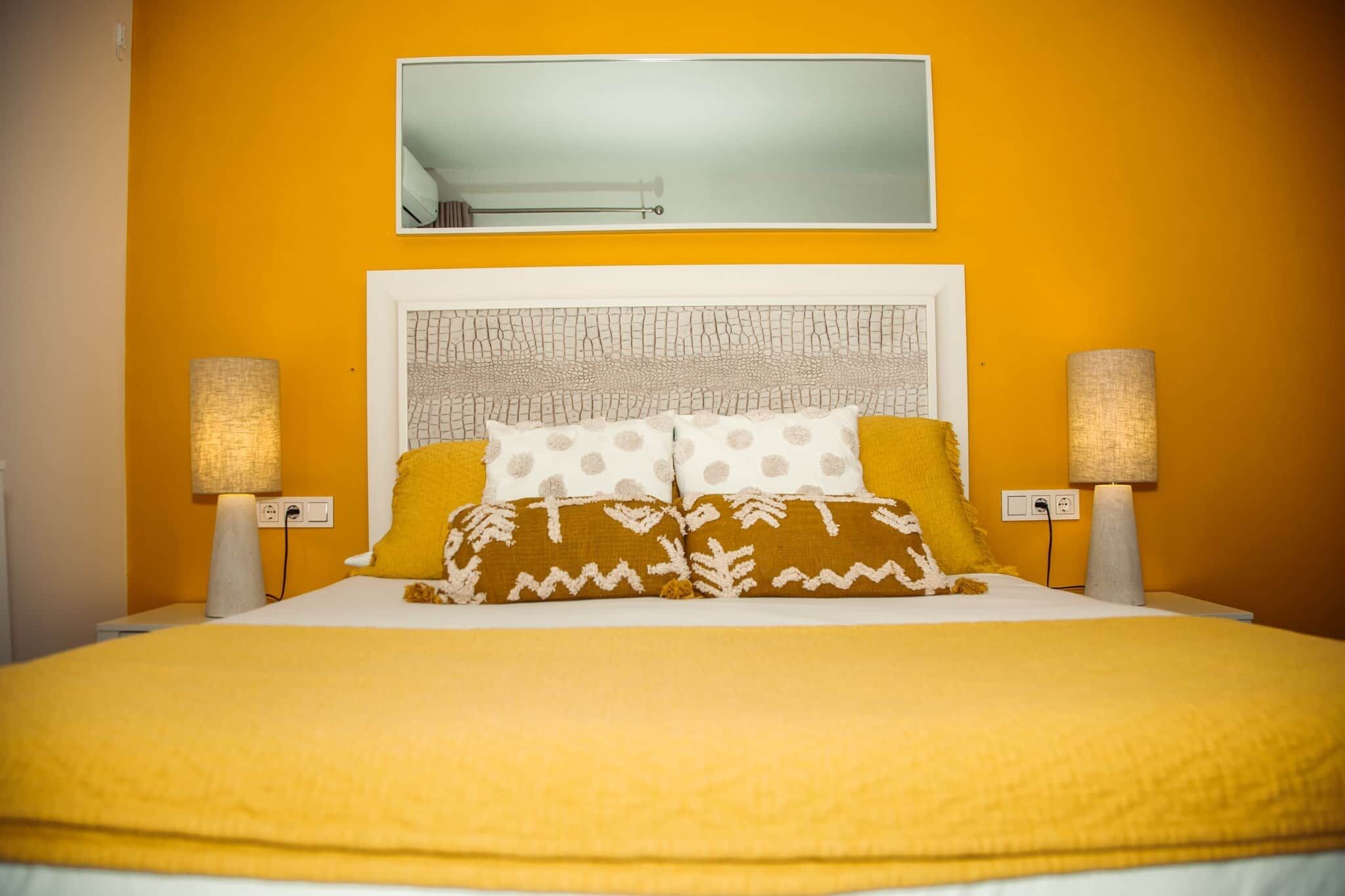 Un lit avec une tête de lit blanche, deux lampes de chevet et une couvre-lit jaune.