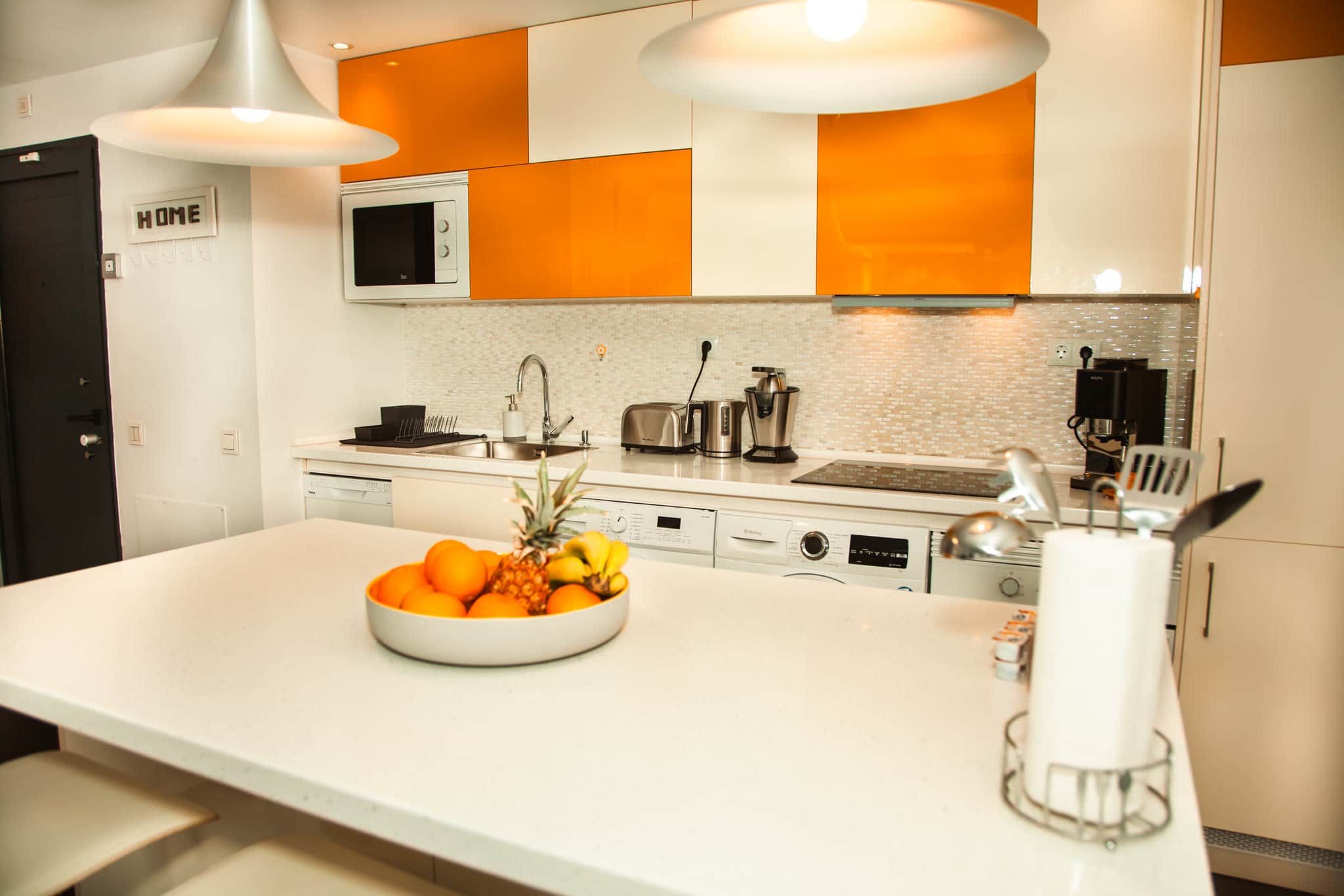 Une cuisine moderne avec un îlot central, un four à micro-ondes placé au-dessus de l’évier et un grille-pain sur le plan de travail.
