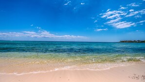 Une plage à l’eau turquoise et limpide, un rivage sablonneux et, au loin, une île parsemée de bâtiments.