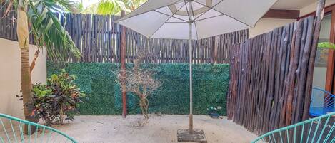 Un espace patio aménagé avec une table en bois, deux chaises, un fauteuil suspendu et un grand parasol.