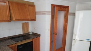 A kitchen with wooden cabinets, a granite countertop, a dishwasher, a refrigerator, and a door with a frosted glass panel. - Les Motes 2º Solo Familias! (Xeraco Playa)