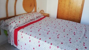 A bedroom with a wooden headboard, a wooden wardrobe, and a bed with patterned bedding. - Les Motes 2º Solo Familias! (Xeraco Playa)