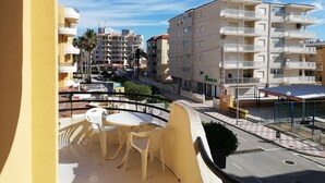 A balcony with a table and chairs, overlooking a street with buildings and a pharmacy. - Les Motes 2º Solo Familias! (Xeraco Playa)