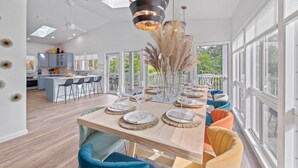 A modern kitchen with a central island, large windows, and a dining area with colorful chairs.