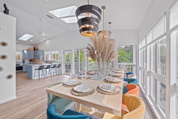 A modern kitchen with a central island, large windows, and a dining area with colorful chairs.