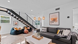 A modern living room with a staircase, a gray sofa, a white coffee table, and a large window.