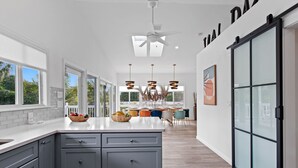 A modern kitchen with grey cabinets, a large island with fruit bowls, and a dining area with colorful chairs.