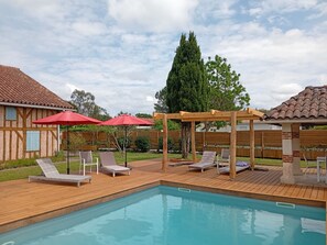 A backyard with a swimming pool, wooden deck, lounge chairs, and red umbrellas. - Villa 230 M2 With Garden  Lac De Léon And Ocean (Léon)